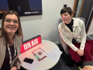 Sian and Eve sat by and 'On Air' sign at the BBC Somerset Studio.